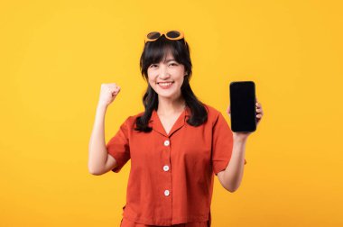 Portre güzel Asyalı kadın mutlu bir gülümseme turuncu giysiler içinde akıllı telefon ve el hareketi ile sarı stüdyo arka planda izole. uygulama akıllı telefon kavramı