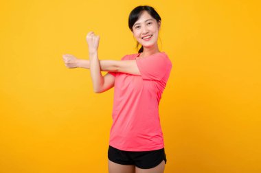 Genç, güzel Asyalı spor spor zeminli kadın mutlu bir gülümseme takınıyor pembe spor kıyafetleriyle egzersiz yapıyor sarı arka planda izole edilmiş. Refah ve sağlıklı yaşam tarzı kavramı.