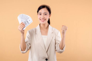 Beyaz ceketli mutlu, kendine güvenen Asyalı iş kadınının portresi. Elinde para var ve bej arka planda duruyor. Milyoner işi, alışveriş konsepti.