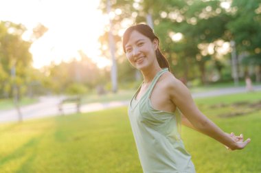 Kadın koşucu. Açık havada koşup eğlenmeden önce yeşil spor kıyafetli sağlıklı Asyalı genç bir kadın parkta temiz hava soluyor. Kamu parkındaki spor koşucusu kız. Refah konsept demek.