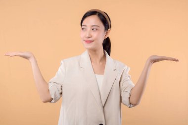 Başarılı, kendinden emin Asyalı genç iş kadınının stüdyo portresi. Beyaz ceketli güzel bir bayan kameraya gülümsüyor. Katı bej renkli arka planda tek başına duruyor.