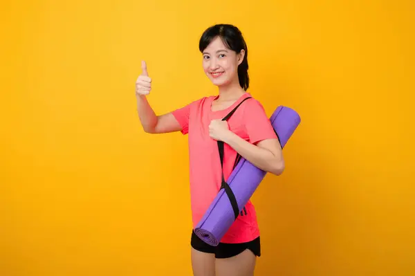 Portrait asian young sports fitness woman happy smile wearing pink sportswear and yoga mat doing exercise training workout against yellow studio background. Healthy wellness lifestyle concept.