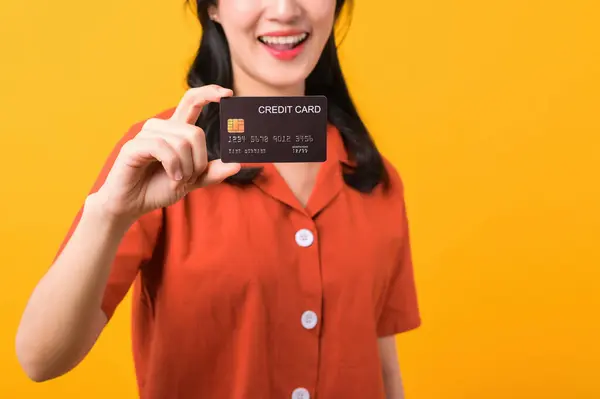肖像画美しい若いアジアの女性は黄色の背景に隔離されたクレジットカードを示すオレンジ色の服を着た幸せな笑顔 支払いとショッピング決済のコンセプト — ストック写真