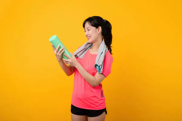 Portrait asian young sports fitness woman happy smile wearing pink sportswear and face towel doing exercise training workout against yellow studio background. wellbeing and healthy lifestyle concept.