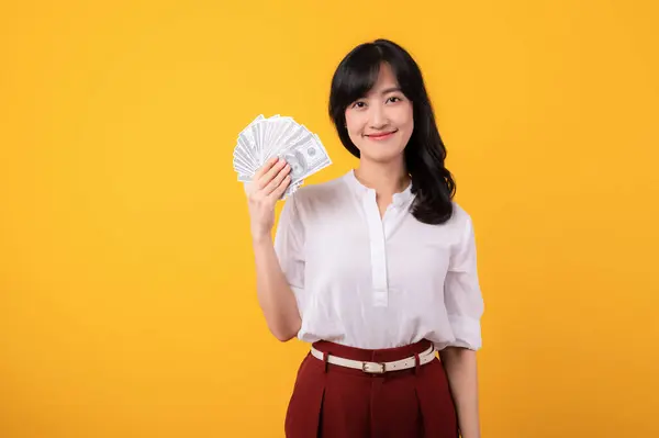 年轻美丽的亚裔女企业家的画像 穿着白衬衫 头戴红色的植物 背景为黄色 背景为金钱隔离 面带微笑 资金在线支付概念 — 图库照片