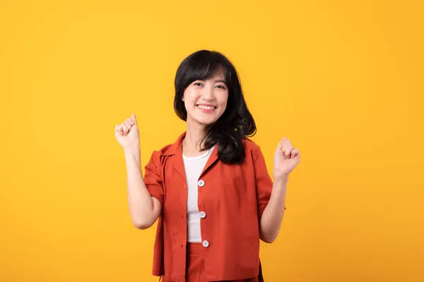 在黄色的工作室背景下 穿着橙色衣服的美丽的年轻亚洲女人脸上挂着幸福的笑容 露出拳头向上的手势 成功地庆祝年轻人的概念 — 图库照片