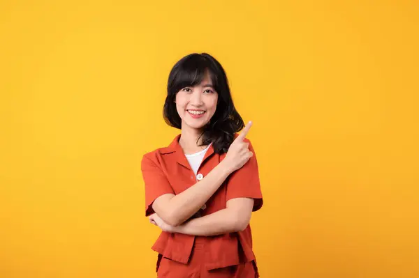 穿着橙色衣服的美丽的年轻的亚洲女人脸上挂着幸福的笑容 用手指指尖的手势表示在黄色工作室背景下与世隔绝的自由空间 注意好的产品 — 图库照片
