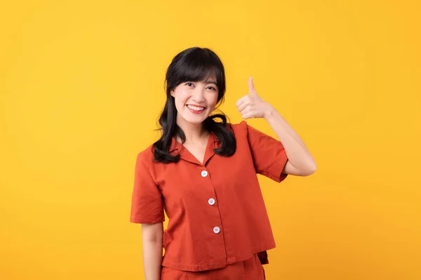 肖像画美しい美しい若いアジアの女性は承認で親指を示すオレンジ色の服を着た幸せな笑顔 黄色のスタジオの背景に隔離された臭いのような推薦します — ストック写真