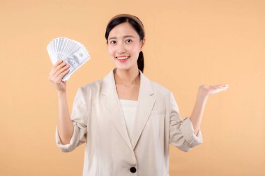 Beyaz ceketli mutlu, kendine güvenen Asyalı iş kadınının portresi. Elinde para var ve bej arka planda duruyor. Milyoner işi, alışveriş konsepti.