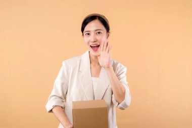 Başarılı, kendinden emin, beyaz ceketli genç Asyalı iş kadınının portresi bej renkli stüdyo arka planında izole edilmiş paket kutusu teslimat kuryesi ve nakliye hizmeti konsepti..