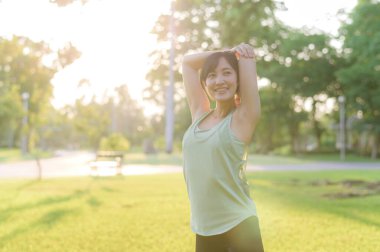 Kadın koşucu. Açık havada koşup eğlenmeden önce yeşil spor kıyafetli sağlıklı bir Asyalı genç kadın parkta kaslarını esnetiyor. Kamu parkındaki spor koşucusu kız. Refah konsept demek.