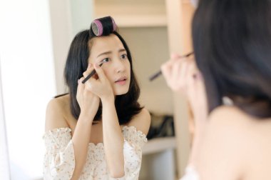 Güzel Asyalı genç bir kadın aynanın önünde makyaj yapıyor. Yaşam tarzı insan kavramı. Cilt kremi reklamı, kırışıklık önleyici krem, bebek yüzü.