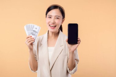 Beyaz ceketli mutlu Asyalı iş kadınının portresi. Elinde akıllı telefon ve nakit para var. Bej arka planda duruyor. Milyoner işi, alışveriş konsepti.