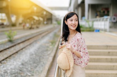 Elinde sepetle tren istasyonunda bekleyen Asyalı genç bir gezgin kadın. Seyahat yaşam tarzı, dünya turisti ya da Asya yaz turizmi konsepti.