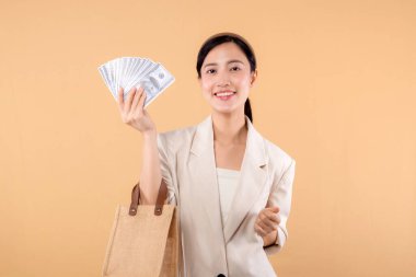 Beyaz ceketli, para dolu beyaz ceketli ve bej arka planda duran başarılı, kendine güvenen genç Asyalı iş kadınının portresi. Çevre dostu alışveriş kavramı.