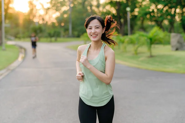 Fit young Asian woman jogging in park smiling happy running and enjoying a healthy outdoor lifestyle. Female jogger. Fitness runner girl in public park. healthy lifestyle and wellness being concept