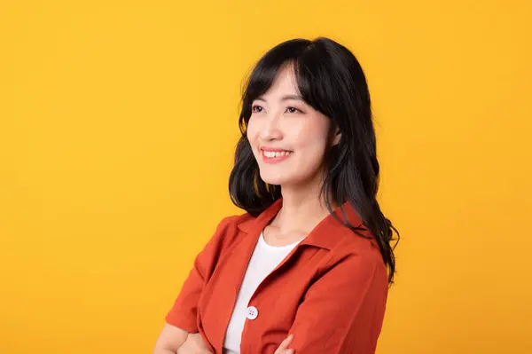 穿着橙色衣服的美丽的年轻亚洲女人快乐地微笑 在黄色的摄影棚背景下表现出思维的姿态 — 图库照片