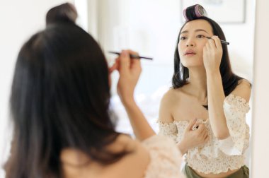 Güzel Asyalı genç bir kadın aynanın önünde makyaj yapıyor. Yaşam tarzı insan kavramı. Cilt kremi reklamı, kırışıklık önleyici krem, bebek yüzü.