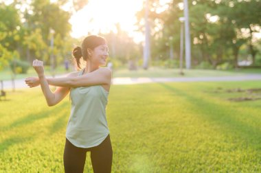 Kadın koşucu. Açık havada koşup eğlenmeden önce yeşil spor kıyafetli sağlıklı bir Asyalı genç kadın parkta kaslarını esnetiyor. Kamu parkındaki spor koşucusu kız. Refah konsept demek.