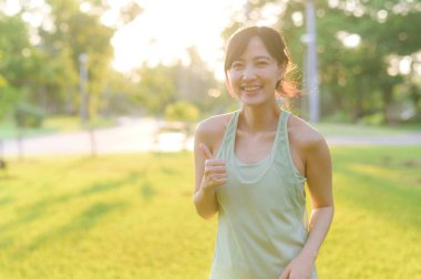 Kadın koşucu. Açık havada koşup eğlenmeden önce yeşil spor kıyafetli sağlıklı bir Asyalı genç kadın parkta kaslarını esnetiyor. Kamu parkındaki spor koşucusu kız. Refah konsept demek.