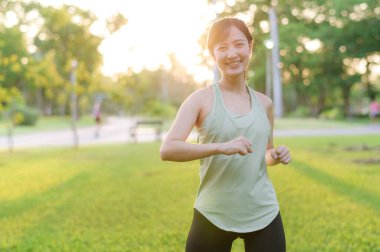 Kadın koşucu. Açık havada koşup eğlenmeden önce yeşil spor kıyafetli sağlıklı bir Asyalı genç kadın parkta kaslarını esnetiyor. Kamu parkındaki spor koşucusu kız. Refah konsept demek.