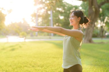 Kadın koşucu. Açık havada koşup eğlenmeden önce yeşil spor kıyafetli sağlıklı bir Asyalı genç kadın parkta kaslarını esnetiyor. Kamu parkındaki spor koşucusu kız. Refah konsept demek.