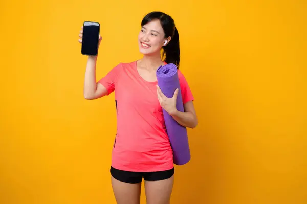 Portrait asian young sports fitness woman happy smile wearing pink sportswear and smartphone doing exercise training workout against yellow studio background. technology wellness lifestyle concept.