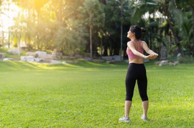 Kadın koşucu. Pembe spor giyim giymiş genç Asyalı bir kadının koşmadan önce parkta kaslarını esnetirken ve dışarıda sağlıklı aktivitelerin keyfini çıkarırken görüntüsünü alın. Doğal ortamdaki sağlık ve zindelik.