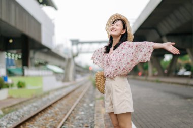 Tren yolunun yanındaki kameraya gülümseyen sepetli Asyalı genç kadın gezgin. Seyahat yaşam tarzı, dünya turisti ya da Asya yaz turizmi konsepti.