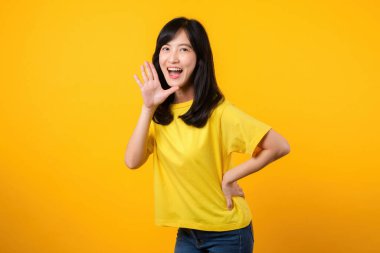 Bu canlı portredeki enerjiyi ve ifadeyi deneyimleyin. Sarı tişört ve kot pantolon giyen genç Asyalı kadın dinamik el hareketi sergiliyor. Heyecan ve heyecan için mükemmel..