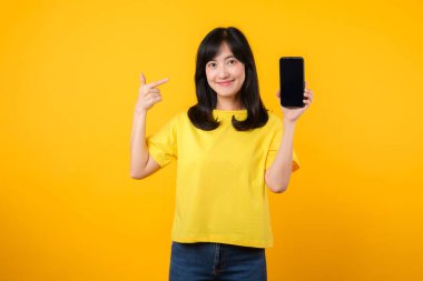 Sarı t-shirt ve kot pantolon giyen neşeli Asyalı genç kadın akıllı telefonu işaret ederek yeni uygulamaların neşe ve heyecanını yakalayın. Uygulama ve dijital yenilik kavramı.