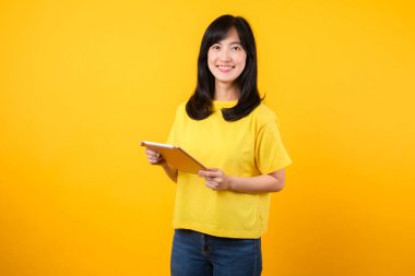 Eğitim teknolojisinin zevkini portre ile yaşayın. Sarı tişört ve kot pantolon giyen Asyalı genç bir kadın dijital tablet kullanırken mutlu bir gülümseme sergiliyor. eğitim teknolojisi kavramı.