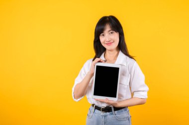Kendinden emin Asyalı kadın dijital çağı kucaklıyor, elinde parlak sarı arkaplanda tablet tutuyor. Modern bağlantı, teknoloji meraklılığı ve güçlendirme. dijital yaşam tarzları ve teknolojik gelişmeler.