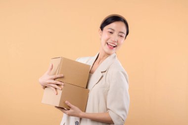 Başarılı, kendinden emin, beyaz ceketli genç Asyalı iş kadınının portresi bej renkli stüdyo arka planında izole edilmiş paket kutusu teslimat kuryesi ve nakliye hizmeti konsepti..