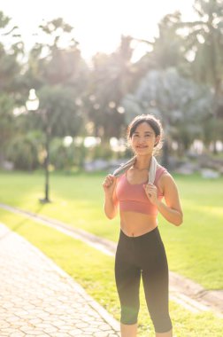 Mutlu bir gülümseme 30 'lu yaşlardaki spor giysili Asyalı genç kadın doğada günbatımının ferahlatıcı tadını çıkarıyor. Batan güneşe karşı siluet çok güzel bir manzara. Fitness, sağlık veya motivasyon kavramı.