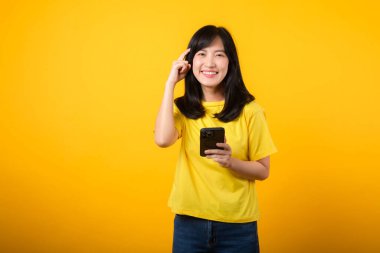 Etkileyici bir portre ile duyguların deneyim aralığı. Sarı tişört ve kot pantolon giyen Asyalı genç kadın akıllı telefon kullanırken şüpheli bir ifade sergiliyor. Çeşitli duygular ve teknolojik kullanım.