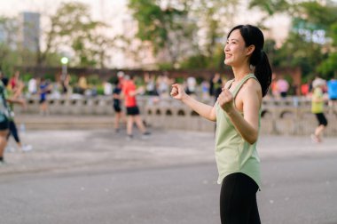 Kadın koşucu. Yeşil spor giyim aerobiği olan formda bir Asyalı genç kadın parkta dans ediyor ve açık havada eğleniyor. Kamu parkındaki spor koşucusu kız. Refah konsept demek.