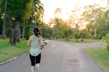 Genç, zinde Asyalı bir kadın parkta koşuyor mutlu bir şekilde koşuyor ve sağlıklı bir açık hava yaşam tarzının tadını çıkarıyor. Kadın koşucu. Kamu parkındaki spor koşucusu kız. Sağlıklı yaşam tarzı ve refah kavramı