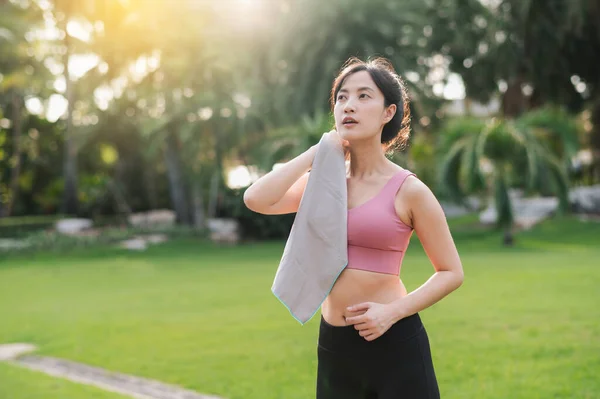 Confident 30s Asian young woman in pink sportswear wipes brow after sunset workout in nature. Captures beauty of healthy lifestyle and perfect for any project promoting fitness, health, or motivation.
