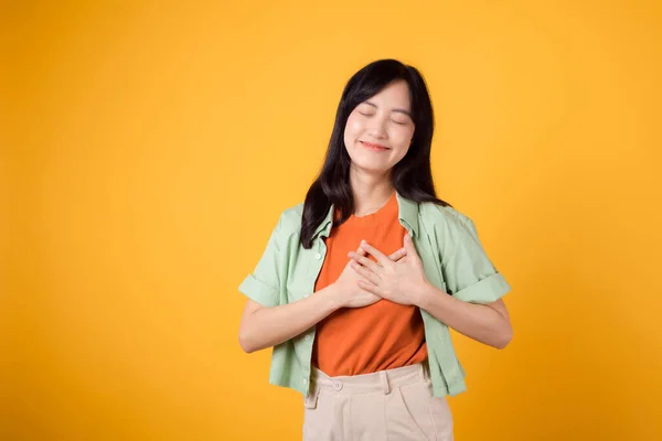 肖像画の喜びは 黄色の背景に隔離された胸に手を握っている若いアジアの女性に感謝します 平和的で感謝の感情 幸福は肯定的な感情を愛する — ストック写真