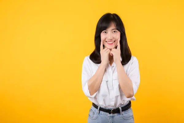 若いアジアの美しい女性は 白いシャツを着て幸せな笑顔と黄色い隔離された背景の上にジーンズの植物は自信を持って示し 指の歯と口を指差しています 歯科コンセプト — ストック写真