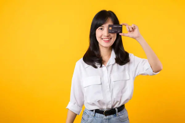 黄色い背景で孤立した幸せな笑顔で片目の前でクレジットカードを持っている若いアジアの女性 支払い オンラインショッピングコンセプト — ストック写真