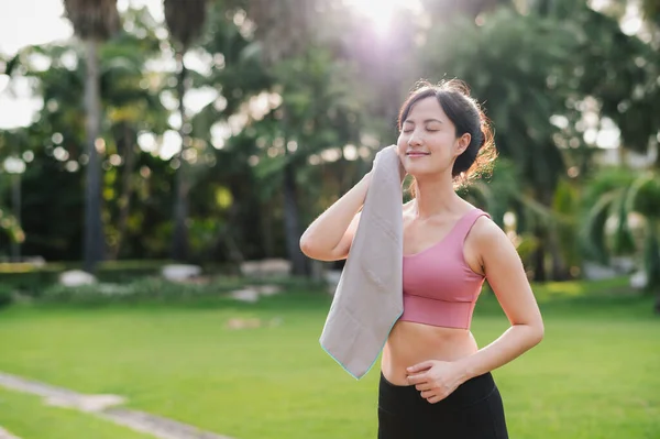 Confident asian 30s woman in pink sportswear wipes her cheek after sunset workout in nature. Captures beauty of healthy lifestyle and perfect for any project promoting fitness, health, or motivation.