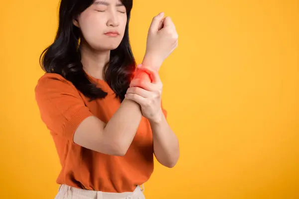 强调关节炎的医疗保健 亚洲30多岁的女人穿着橙色的衬衫 同时在疼痛中握住她的手腕 阐明腕关节关节炎的挑战 是健康与健康的概念 — 图库照片