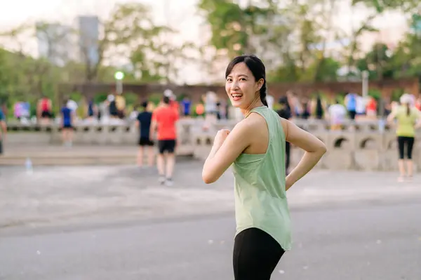 Female jogger. Fit Asian young woman with green sportswear aerobics dance exercise in park and enjoying a healthy outdoor. Fitness runner girl in public park. Wellness being concept