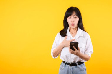 Asyalı genç bir kadının cep telefonunu olumlu bir ifadeyle kullanmasına şaşırdım. Geniş bir şekilde gülümsüyor, beyaz gömlek giyiyor ve sarı arka planda tek başına duruyor. Mutlu, mutlu, mutlu kadın başarıya sevinir..