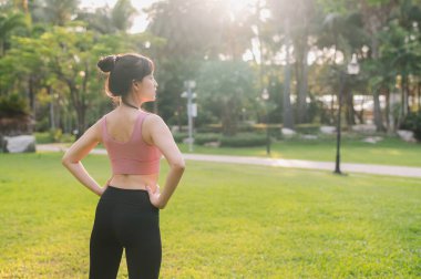 Doğada mutlu, formda, 30 'lu yaşlarda bir Asyalı kadın olarak gün batımından önce vücudunu halka açık bir parkta, pembe spor kıyafetleriyle ısıtırken sıhhatini kucaklayın..