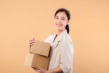Başarılı, kendinden emin, beyaz ceketli genç Asyalı iş kadınının portresi bej renkli stüdyo arka planında izole edilmiş paket kutusu teslimat kuryesi ve nakliye hizmeti konsepti..
