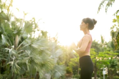 Sağlık konsepti ve sağlıklı olmak 30 'lu yaşlarda pembe spor giyimli genç Asyalı kadın yoga yapıyor ve kaslarını esnetiyor. Gün batımında halka açık parkta sağlıklı bir yaşam tarzını yoga kızıyla kucaklayın..