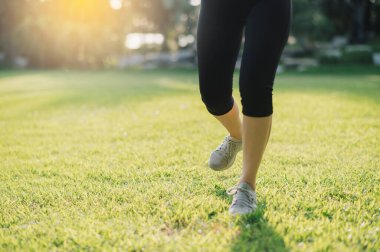 Sağlıklı yaşam kavramını benimse. Gün batımında halka açık bir parkta koşarken kadın koşucunun bacaklarının ve ayakkabılarının yakın plan çekiminin güzelliğini yaşayın..